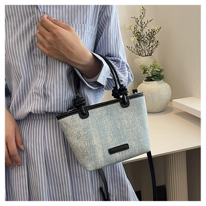 Detail of light blue denim tote bag with black leather trim and cylindrical top handles