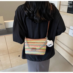 Detail of colorful striped woven straw bucket bag with brown leather strap and plush charm