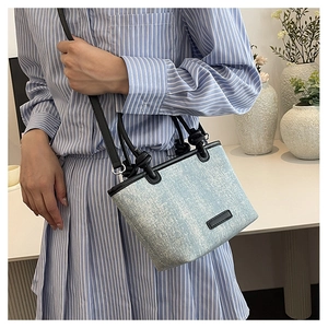 Detail of light blue denim handbag with knotted black leather handle and crossbody strap