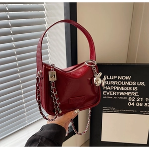 Détail d'un sac à main en cuir verni rouge foncé avec chaîne et pendentif argenté