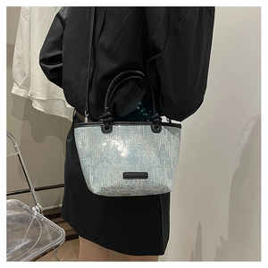 Detail of sequined bucket bag with black handles shown on a shoulder for scale