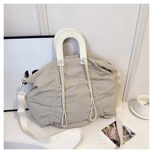 Detail of beige pleated canvas tote bag with curved handle and wide crossbody strap