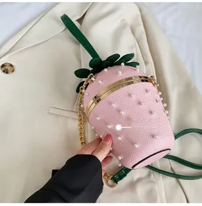 Detail of pink strawberry bucket bag featuring pearl accents and gold metal chain strap