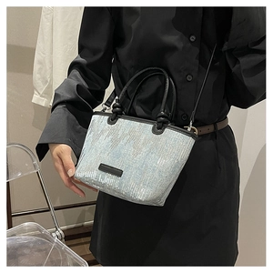 Detail of silver sequins on blue denim bucket bag with black handles and shoulder strap