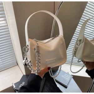 Détail du sac à main crème en cuir verni avec chaîne argentée et breloque chien
