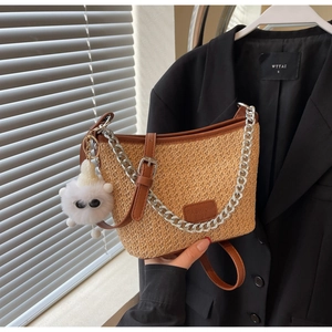 Straw bucket bag with dark brown leather trim, silver chain, and plush bear charm detail