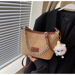 Detail of straw bucket bag with brown leather trim, silver chain and plush charm