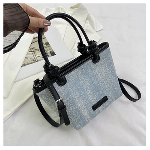 Detail of light blue denim tote with sparkling glitter, black leather handles and strap