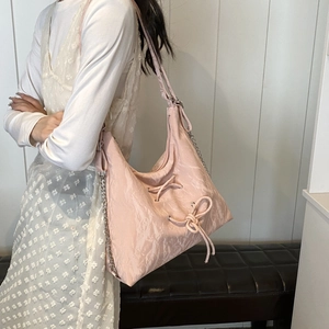 Detail view of pink pleated shoulder bag with bow drawstring and silver chain on model