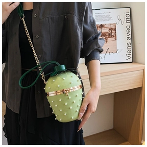 Model wearing a green strawberry-shaped crossbody bag with pearls and a gold chain strap