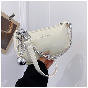 Détail d'un sac à bandoulière blanc cassé avec chaîne argentée et breloque sphérique