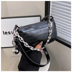 Détail du sac sous le bras en cuir verni noir avec grosse chaîne argentée et bijou