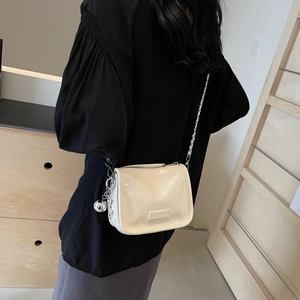Sac sous l'aisselle brillant blanc cassé avec bandoulière chaîne porté par un mannequin