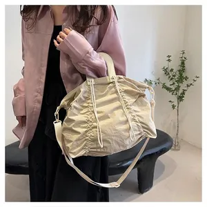 Close-up of a beige pleated canvas crossbody bag with drawstring closure and strap detail