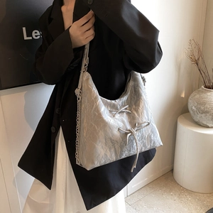Detail of silver pleated hobo bag featuring decorative metal chains and bow knots