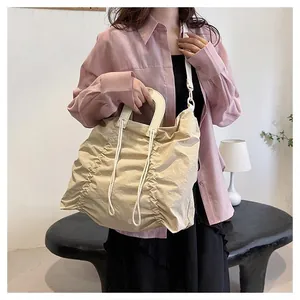 Beige pleated tote bag with drawstring detail and round handle shown with a lifestyle outfit