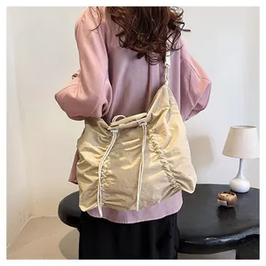 Detail of a large beige pleated crossbody bag with drawstring closure and wide strap