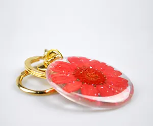 Detail of red dried flower inside oval resin pendant with gold metal keyring and sequins