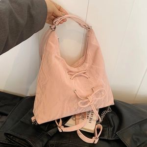 Close-up of pink pleated tote bag featuring decorative bow detail and silver chain strap