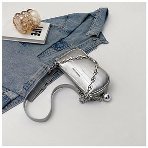 Détail du sac à main argenté avec chaîne, bandoulière en cuir et pendentif sphérique