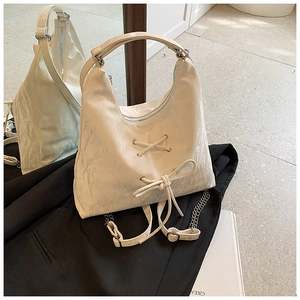 Close-up of cream bow shoulder bag with wrinkled texture and stylish metal chain