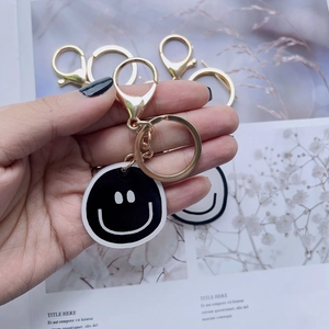 Close-up of black smiley face keychain with golden lobster clasp and ring held by hand