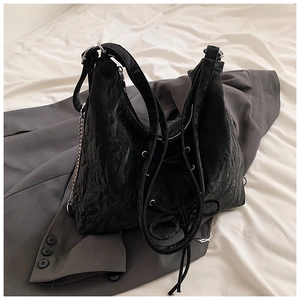 Detail of black pleated tote bag with silver chain straps and decorative lace-up front