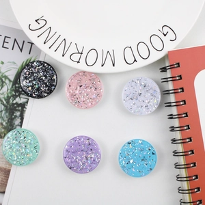 Glitter resin collapsible phone grip stands in six colors displayed on white desk