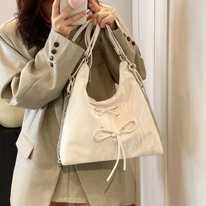 Detail of hobo tote bag featuring a ribbon bow decoration and metallic chain strap