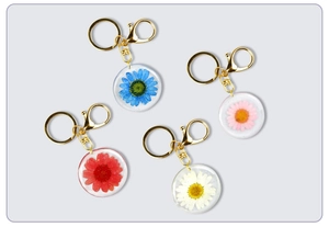 Detailed view of four handmade resin keychains with real dried flowers in gold rings