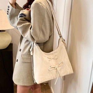 Detail of a beige bow-knot shoulder bag with metallic chain strap worn by a model