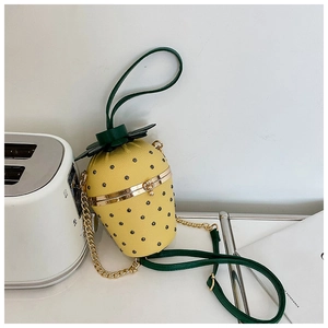 Close-up of a strawberry-shaped yellow crossbody bag with green leaf top and gold chain