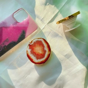 Natural agate stone phone grip with gold rim and red-orange marble texture on white base