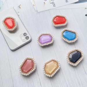 Macro detail of rhinestone and pearl studded gem phone grips on a wooden surface