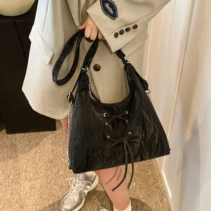 Detail of black pleated leather tote bag with ribbon lacing and silver chain strap