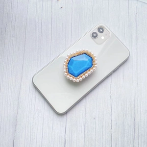 Detailed view of a blue gem phone socket with pearls and rhinestones on a white smartphone