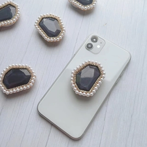 Detail of grey gemstone phone grip with pearl and rhinestone trim on white background