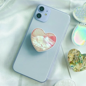 Detail of a heart-shaped phone grip featuring pink shell texture on a purple smartphone