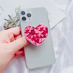 Close-up of a pink glitter heart phone socket grip being held on a white smartphone