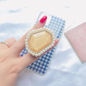 Detailed view of luxury phone grip with yellow gem and pearl embellishments on hand