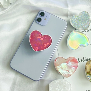 Close-up of heart-shaped phone grips with pearl shell and glitter textures on silk