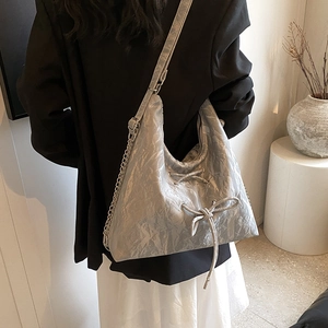 Silver pleated tote bag with bow detail and chain strap worn by a model in a minimal room