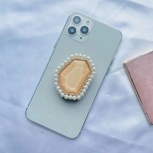 Detailed close-up of a luxury phone grip with orange gem, faux pearls and rhinestones