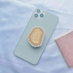 Detailed close-up of a pearl and rhinestone encrusted phone grip with an orange gemstone