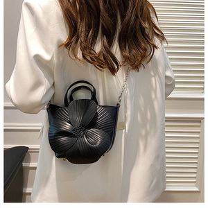Elegant black bucket bag with 3D camellia flower detail worn with white suit
