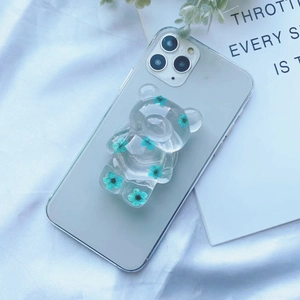 Detail eines transparenten Bären-Handyhalters mit echten blauen Trockenblumen innen
