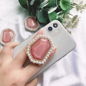Pink gemstone and pearl phone grip stand on a white smartphone with silk backdrop