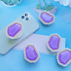 Five purple gem phone sockets with pearls and rhinestones on light blue background