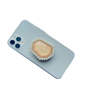 Elegant phone grip with champagne gem, rhinestones, and pearls on a light blue smartphone
