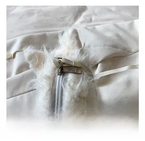 Dettaglio della cerniera in metallo argentato su una borsa a tracolla in peluche bianco